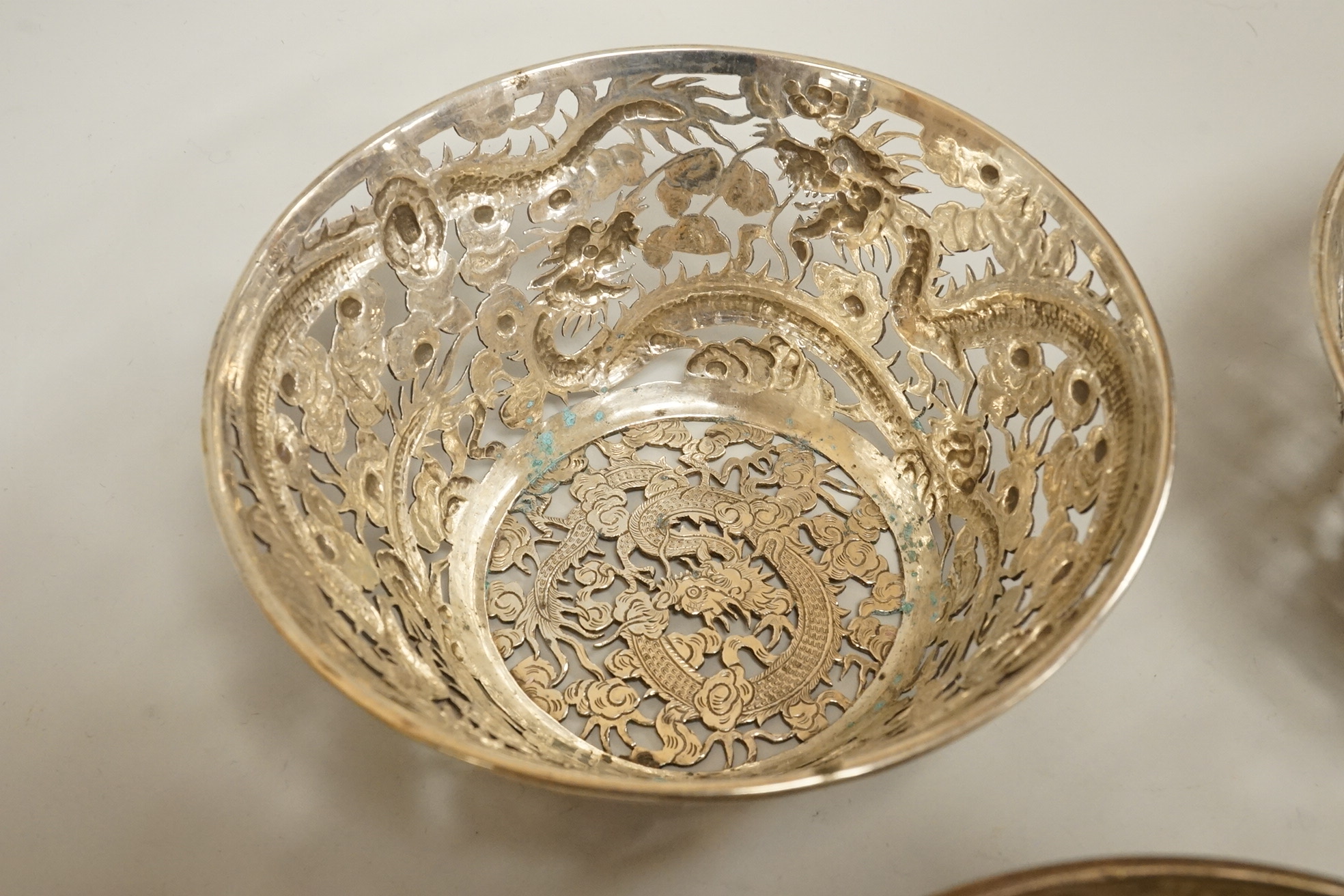 A set of three late 19th/early 20th century Chinese Export pierced white metal bowls, decorated with dragons, by Wang Hing, Hong Kong (lacking glass inserts?), diameter 12.5cm, together with one other similar Chinese Exp